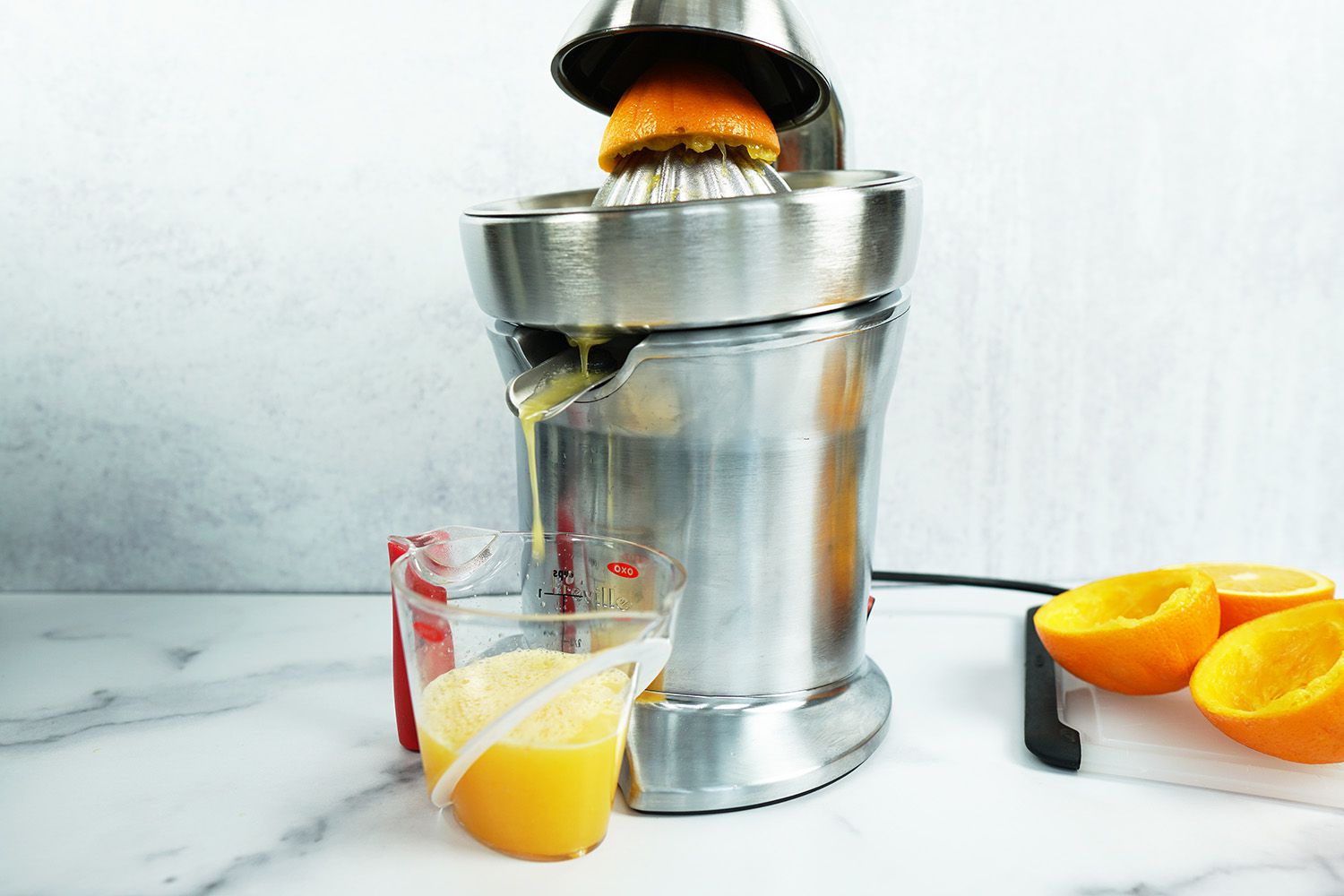 a stainless steel Breville electric citrus juicer juicing orange juice into a measuring cup