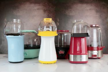 a lineup of six different popcorn makers against a dark background