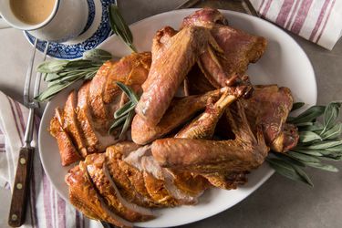 Roasted, carved turkey on a platter with sage leaves. A pitcher of gravy is next to the platter.