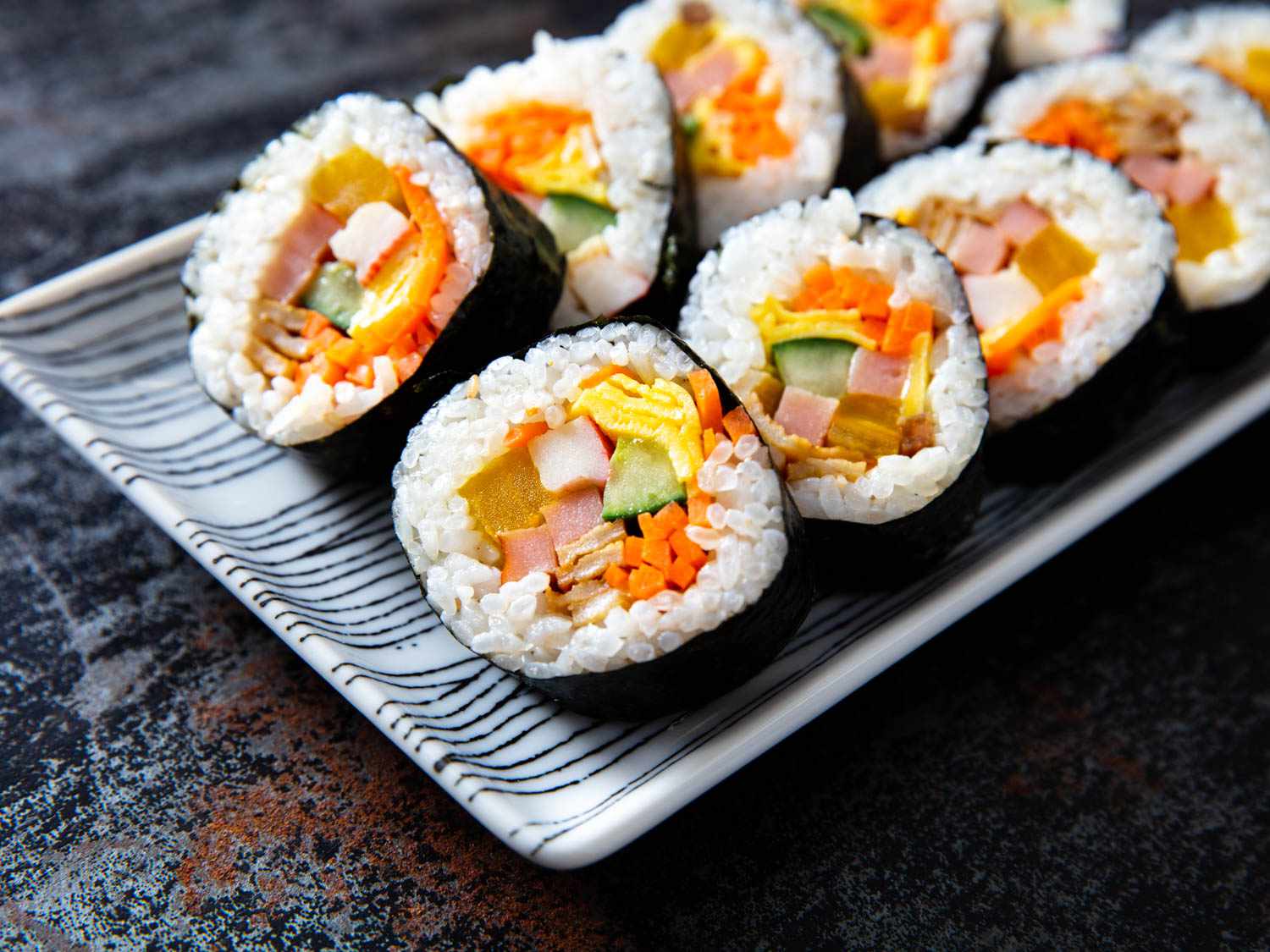 Rows of sliced Korean kimbap - rice wrapped in seaweed sheet (nori), filled with colorful sliced vegetables.