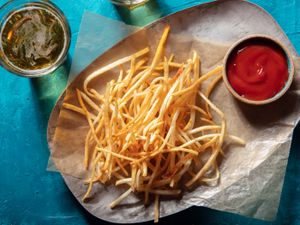 Overhead view of shoestring fries on wax paper on a platter with a ramekin of ketchup and a glass of beer alongside