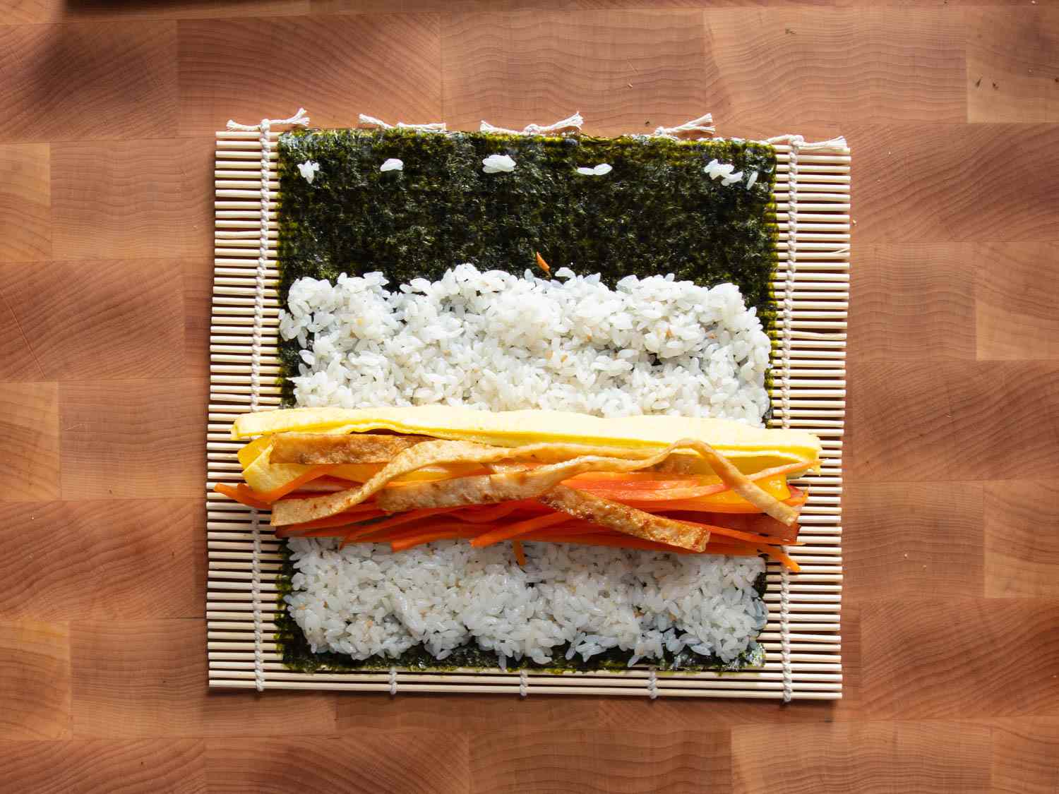Overhead shot of thinly sliced fillings and rice spread out over a sheet of seaweed.