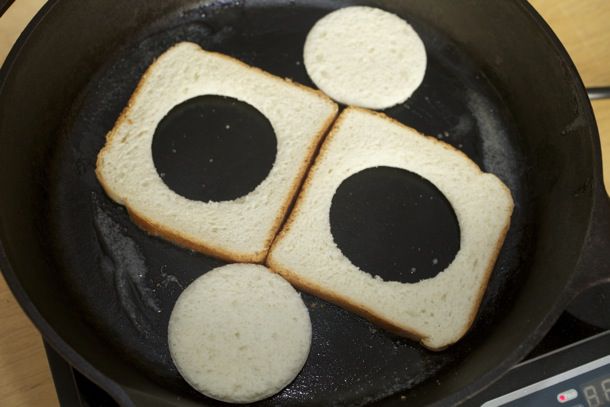 两片切出洞的面包片，外加两个圆形的面包切片，放在煎锅里煎