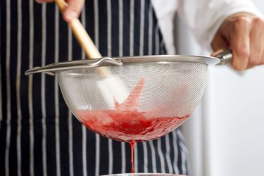 A fine mesh strainer straining strawberry sauce