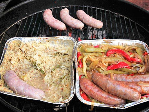 烤架上放着两个铝托盘的香肠(一个装着酸菜和芥末，一个装着辣椒和洋葱)