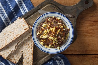 A bowl of chopped liver with matzo crackers on a wooden board.