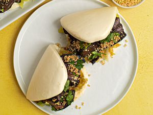 Two Taiwanese pork belly buns (Gua Bao) placed on a white ceramic plate on a yellow background.