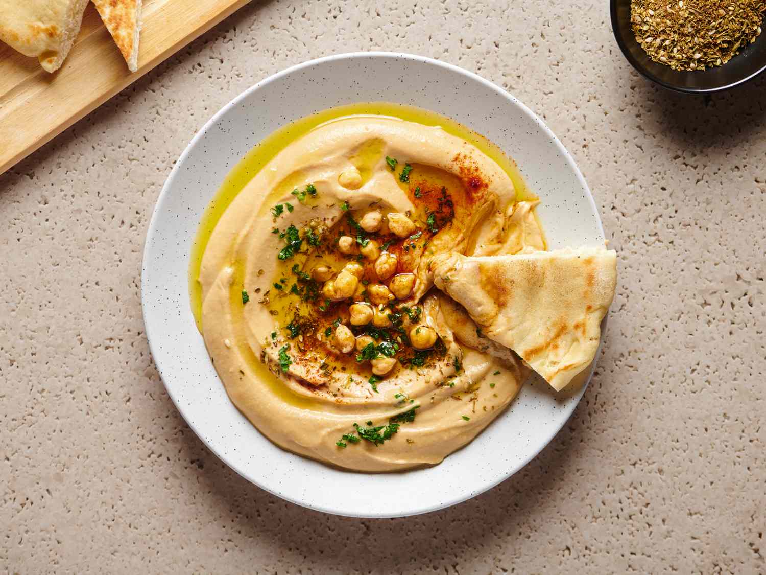 The best smooth hummus in a white round dish, with a piece of pita bread on the right hand side of the plate.