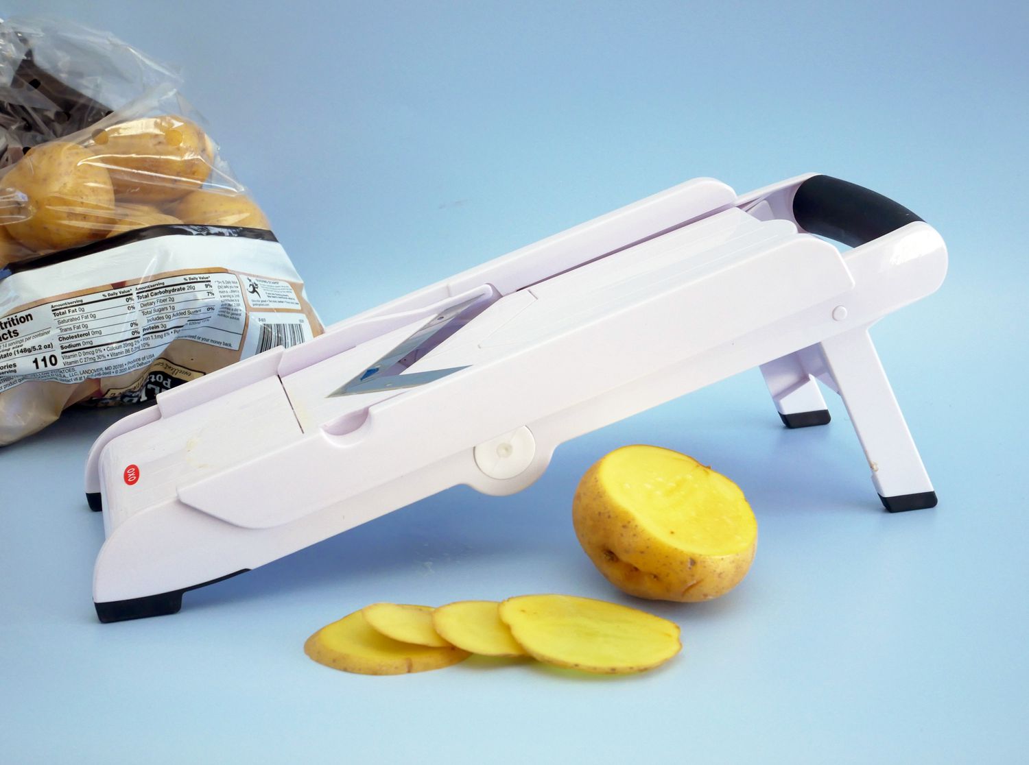 OXO v-blade mandoline with a half-sliced potato in front of it and a bag of potatoes behind it