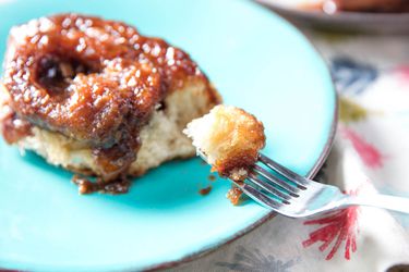 A double-caramel sticky bun on a blue plate with a piece of it on a fork