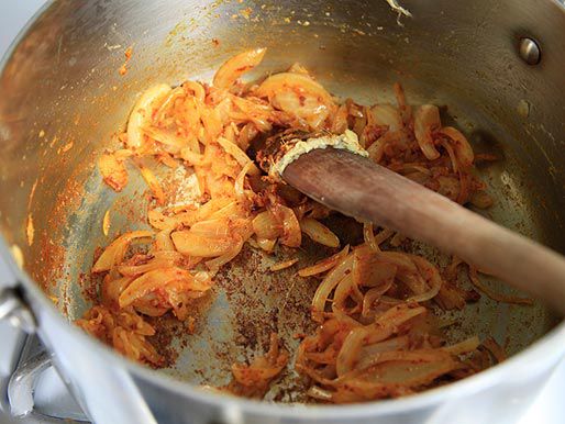 当洋葱在锅中变棕时，用木勺搅拌洋葱和香料。