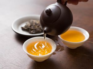 Pu ehr tea being poured from a small black pot into white, handleless cups.