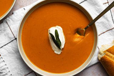 A bowl of butternut squash soup on a dish towel. There is a metal spoon in the bowl.