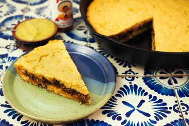 Tamale pie in a cast-iron skillet with a slice of it on a ceramic plate.