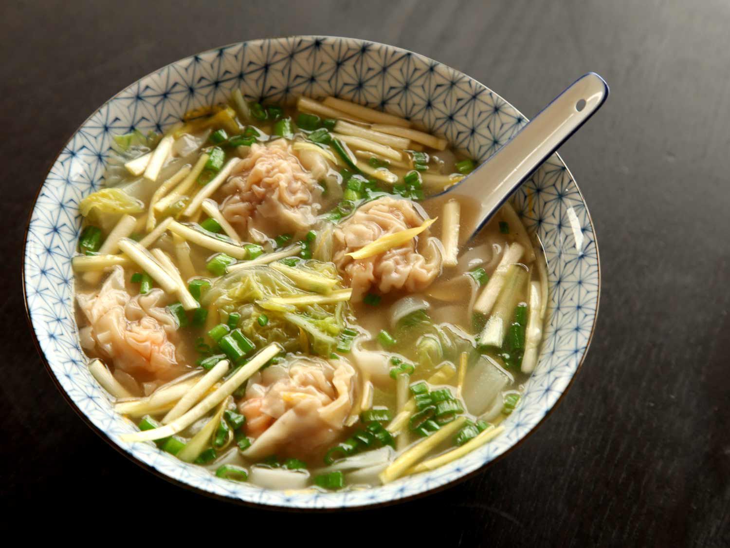 A bowl of wonton soup with a spoon in it.