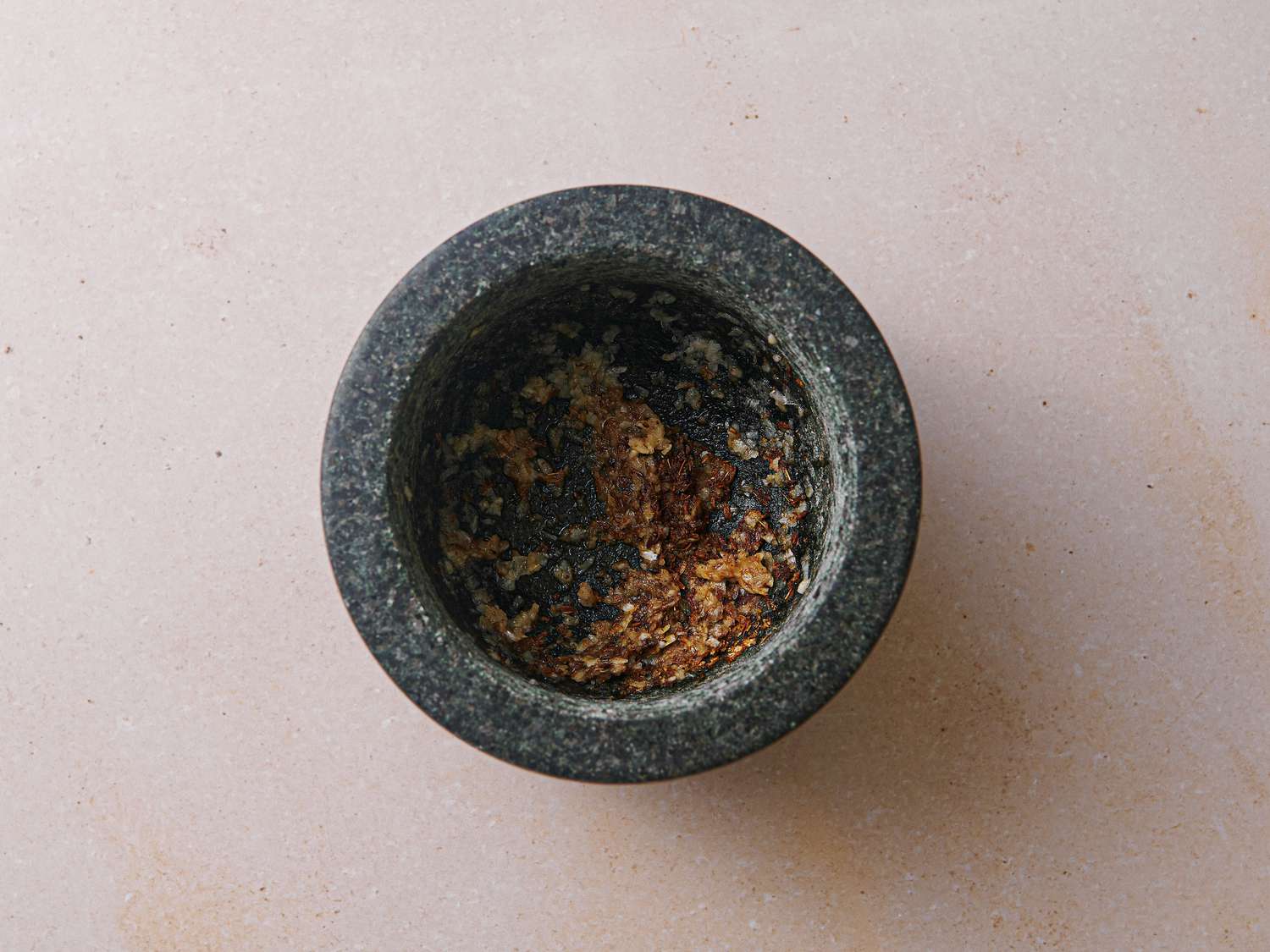 Garlic cloves, cumin seeds, and salt crushed inside mortar