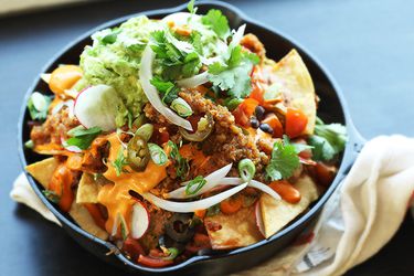 A small cast iron skillet piled with ultimate fully-loaded vegan nachos.