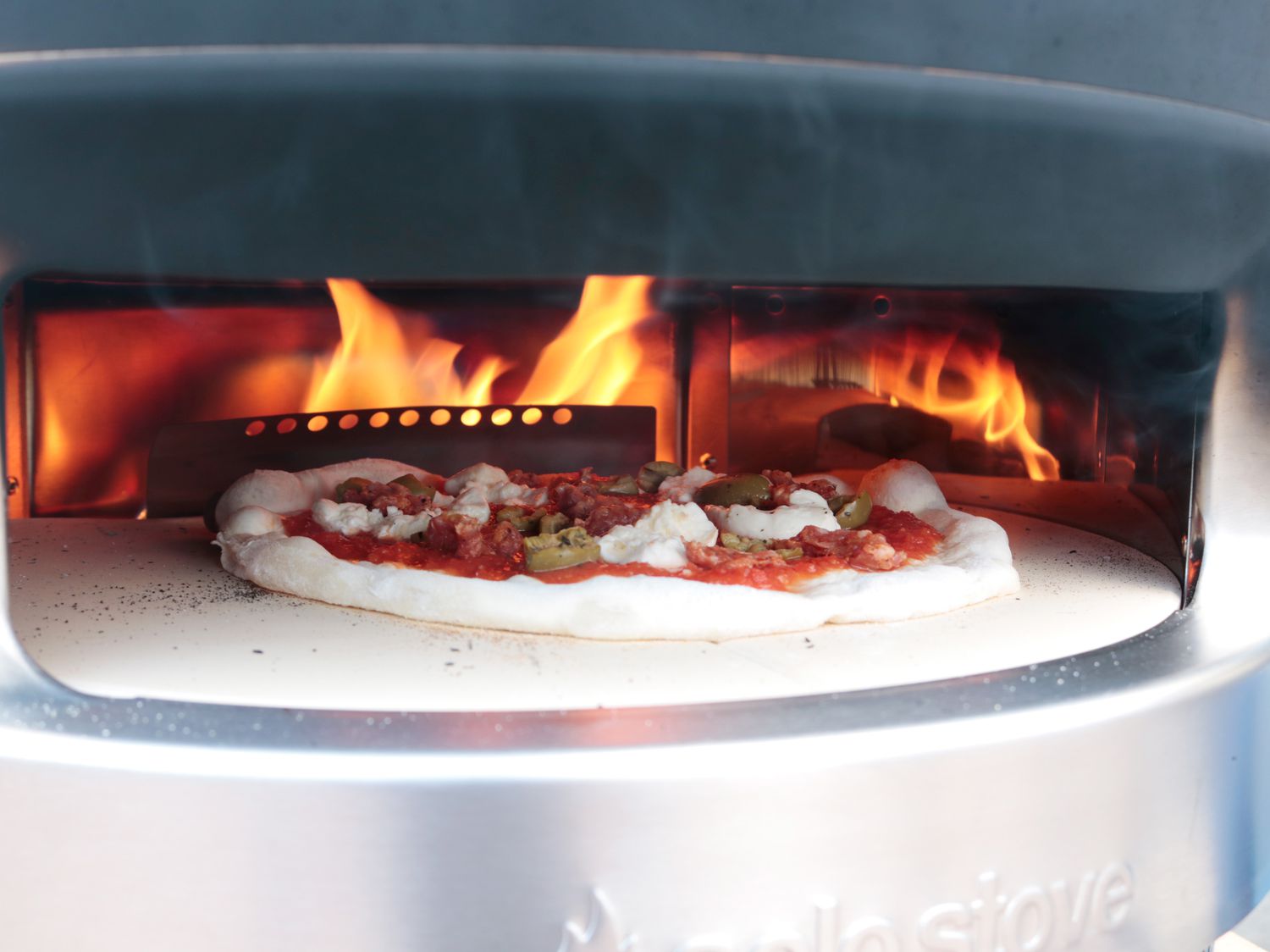 a pizza cooking in front of the metal barrier between the flame and the pizza stone