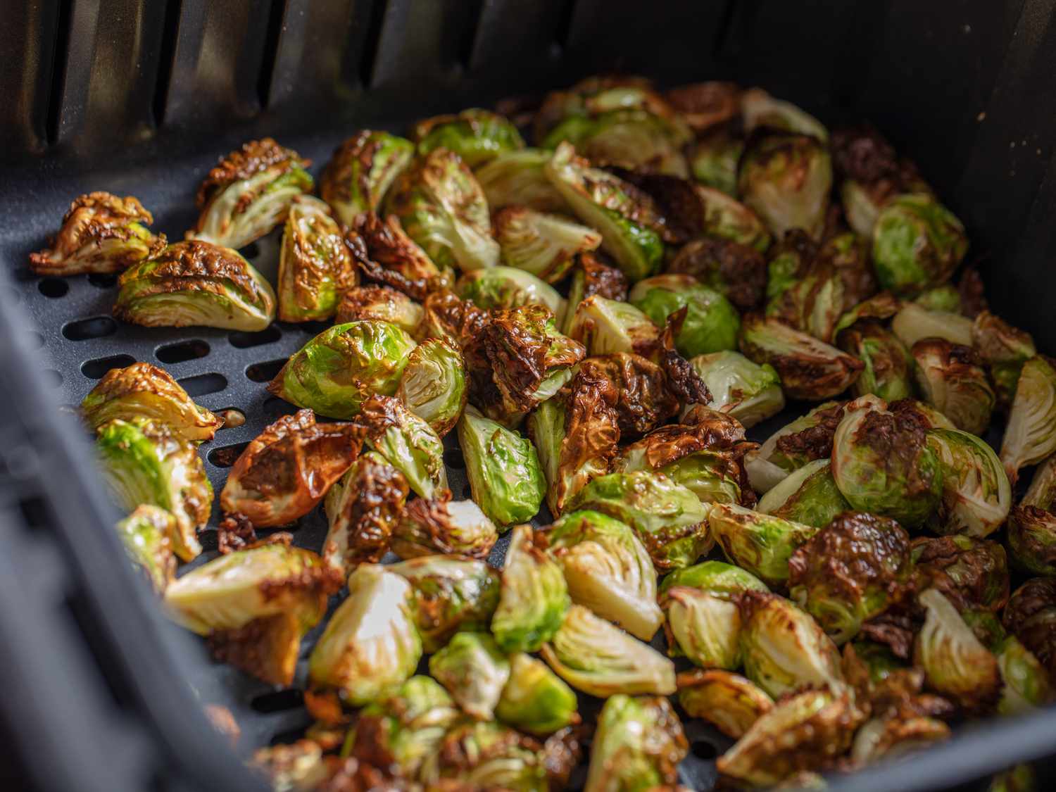 Brussels sprouts quarters in the air fryer basket, showing them golden and crisped all over.