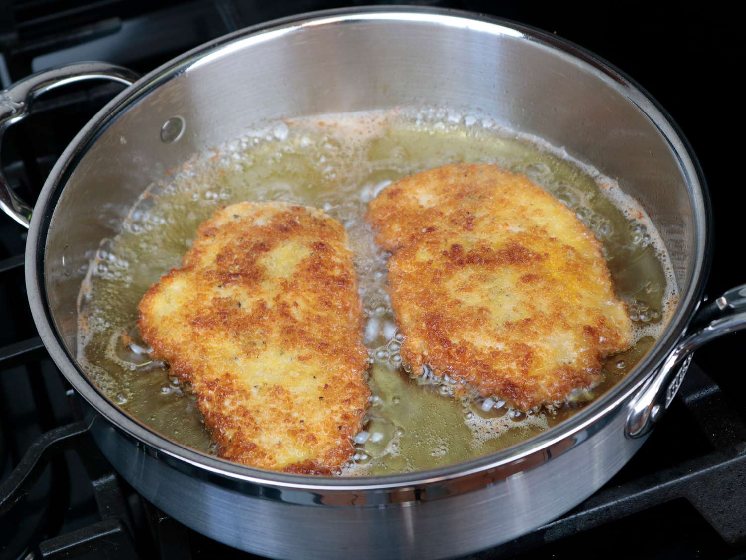 two chicken cutlets frying in oil with a browned side facing up