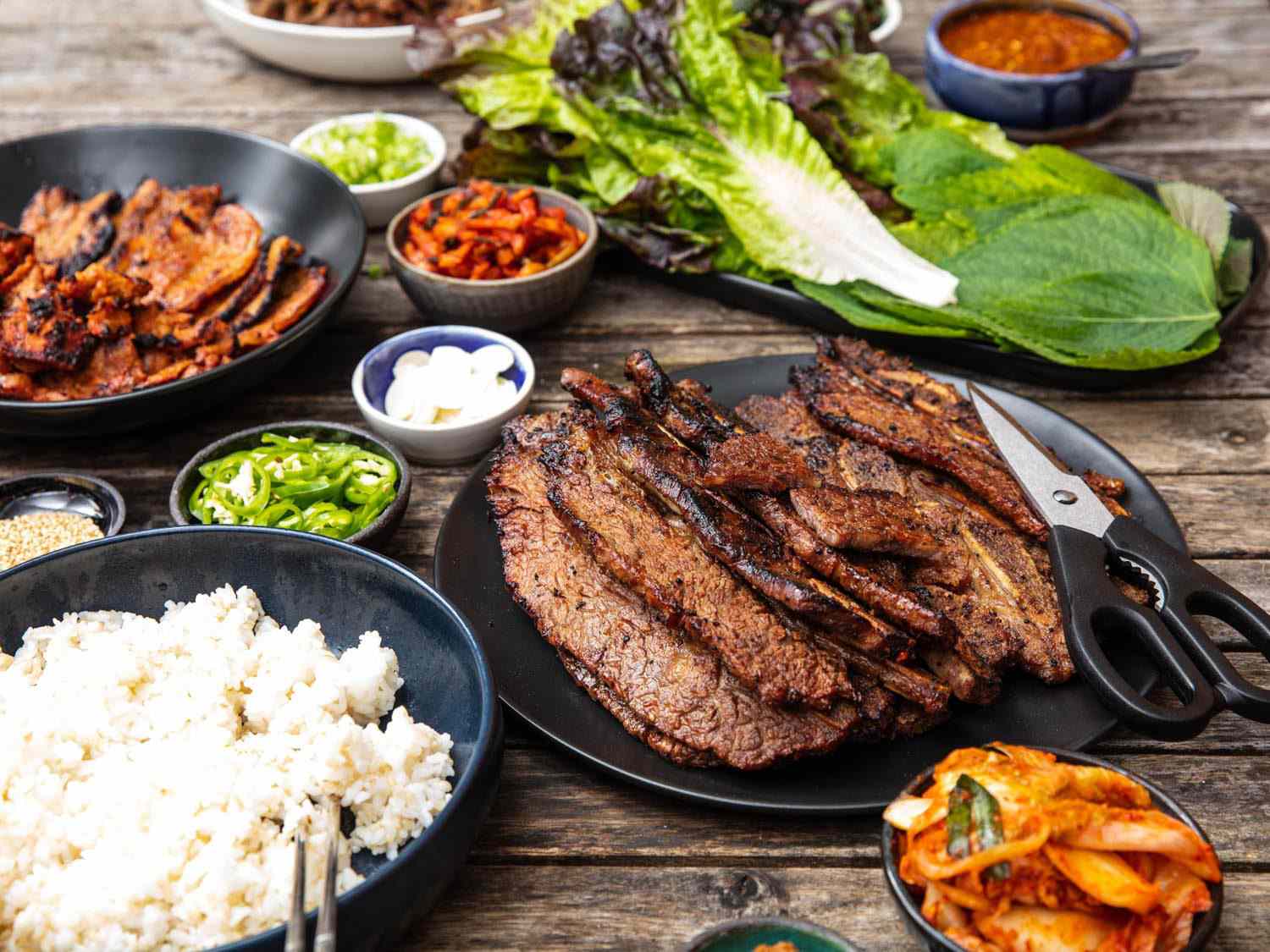 一张桌子的侧面设置了一个韩国烧烤摊，与一盘牛肉galbi在前景。