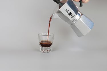 a moka pot pouring coffee into a glaass