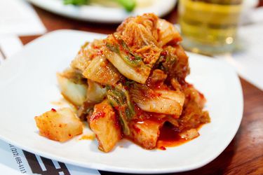 A mound of kimchi on a while plate on a dining table.