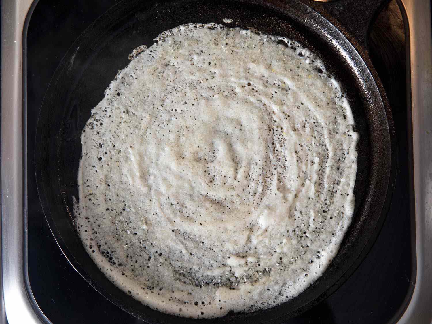 A portion of dosa batter cooking on a griddle.