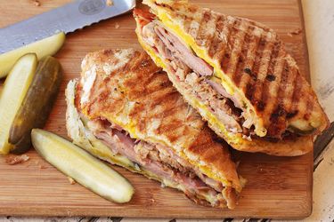 A Cuban sandwich cut in half on a cutting board, with pickle spears next to it.