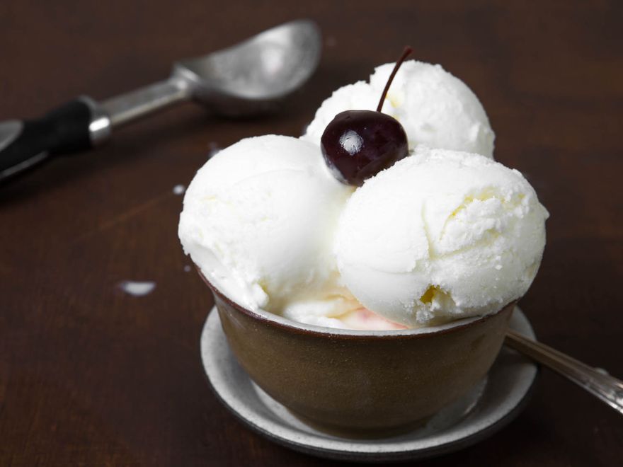 Three scoops of frozen yogurt in a serving glass, garnished with a cherry.