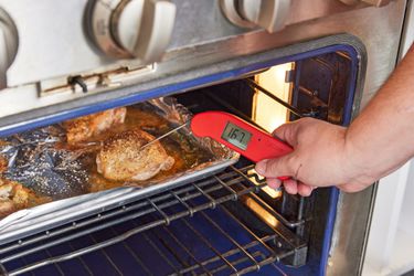 一个人使用thermometer to take the temperature of chicken thighs roasting in the oven