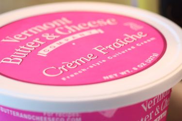 一个粉色和白色的容器crème fraîche的特写。