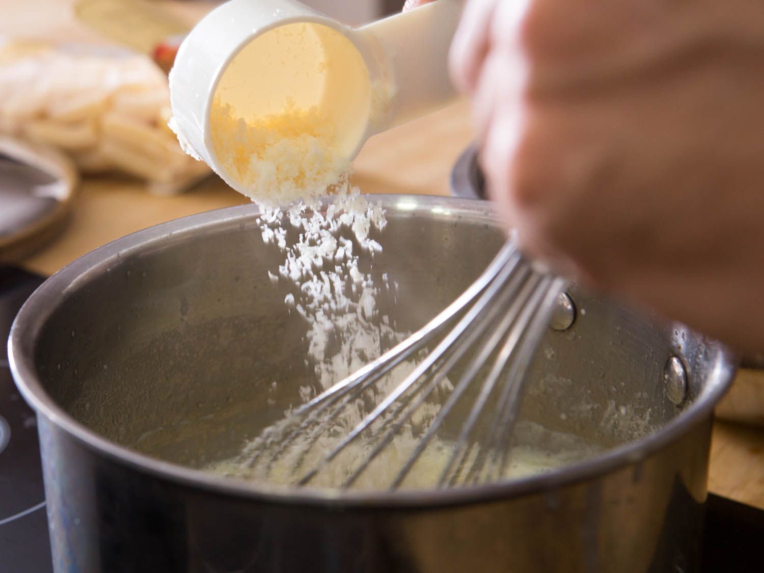 将磨碎的帕尔马干酪撒在一锅奶油酱中。