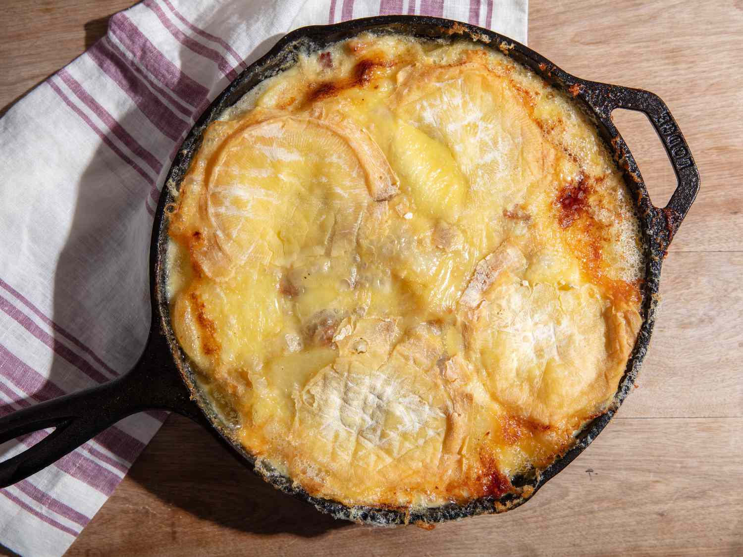 A cast iron skillet full to the brim with melted and browned soft-rind cheese.