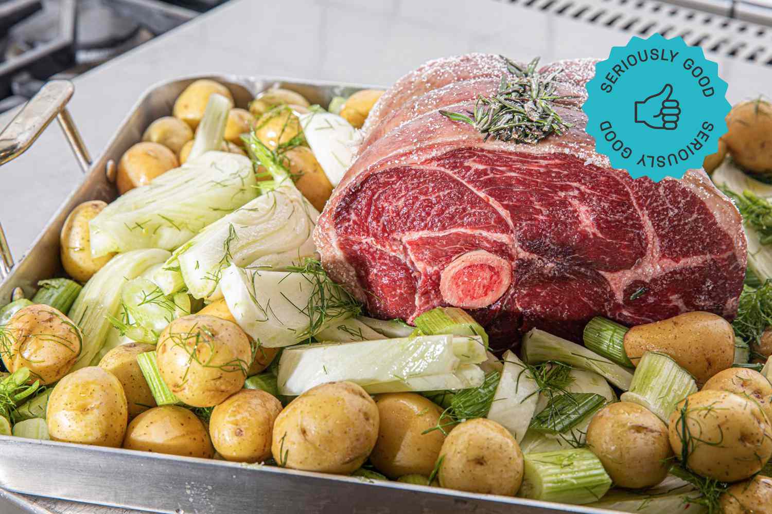 An uncooked roast surrounded by potatoes and fennel and situated in a roasting pan