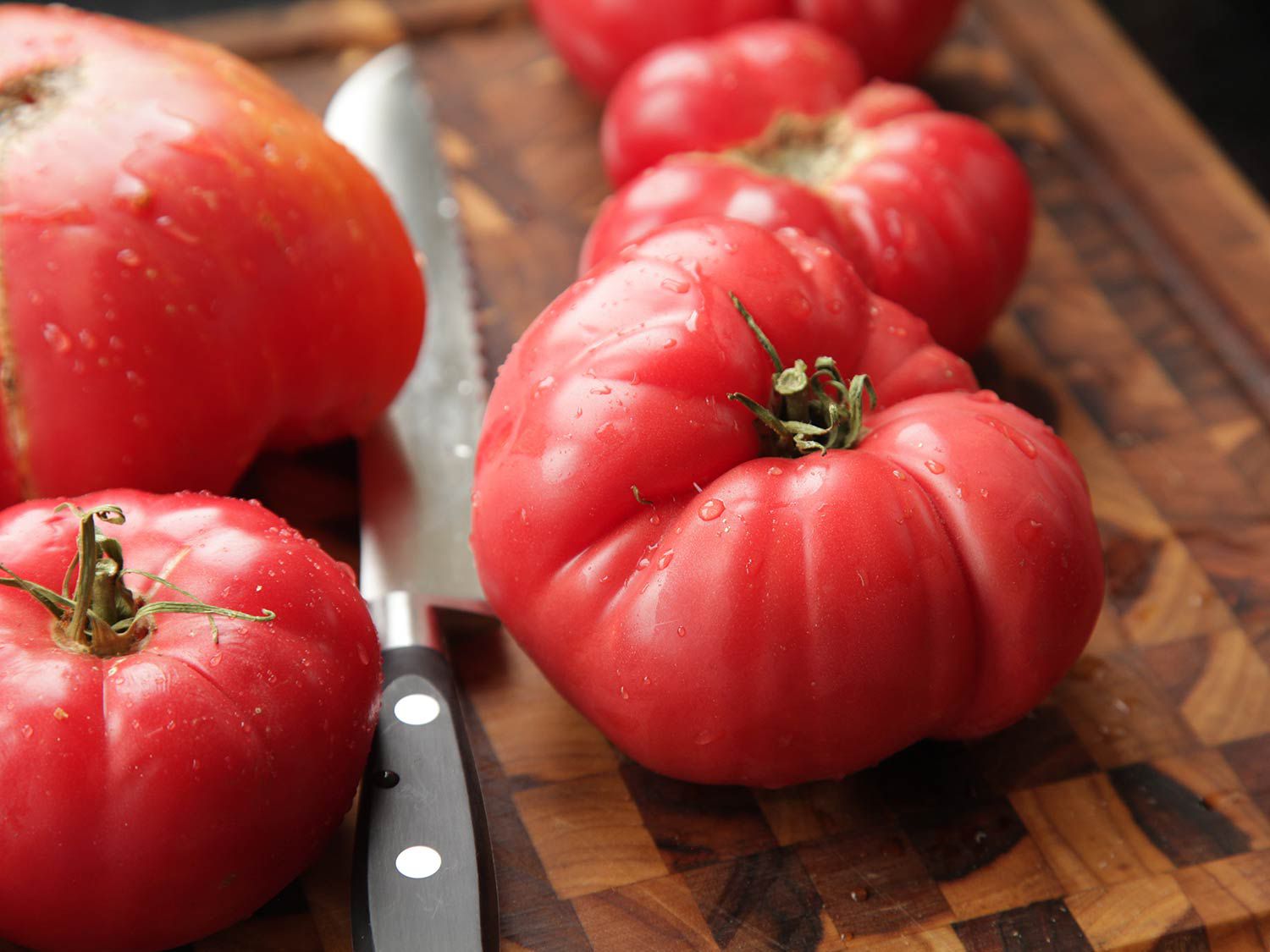 红熟的西红柿放在木砧板上，旁边是一把刀