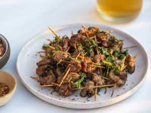 Plate of toothpick lamb set in front of out of focus glass of beer in background