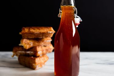 A bottle of homemade pancake syrup next to a stack of waffles.
