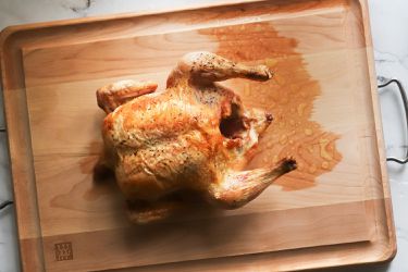 A roast chicken sitting in the center of a wooden carving board