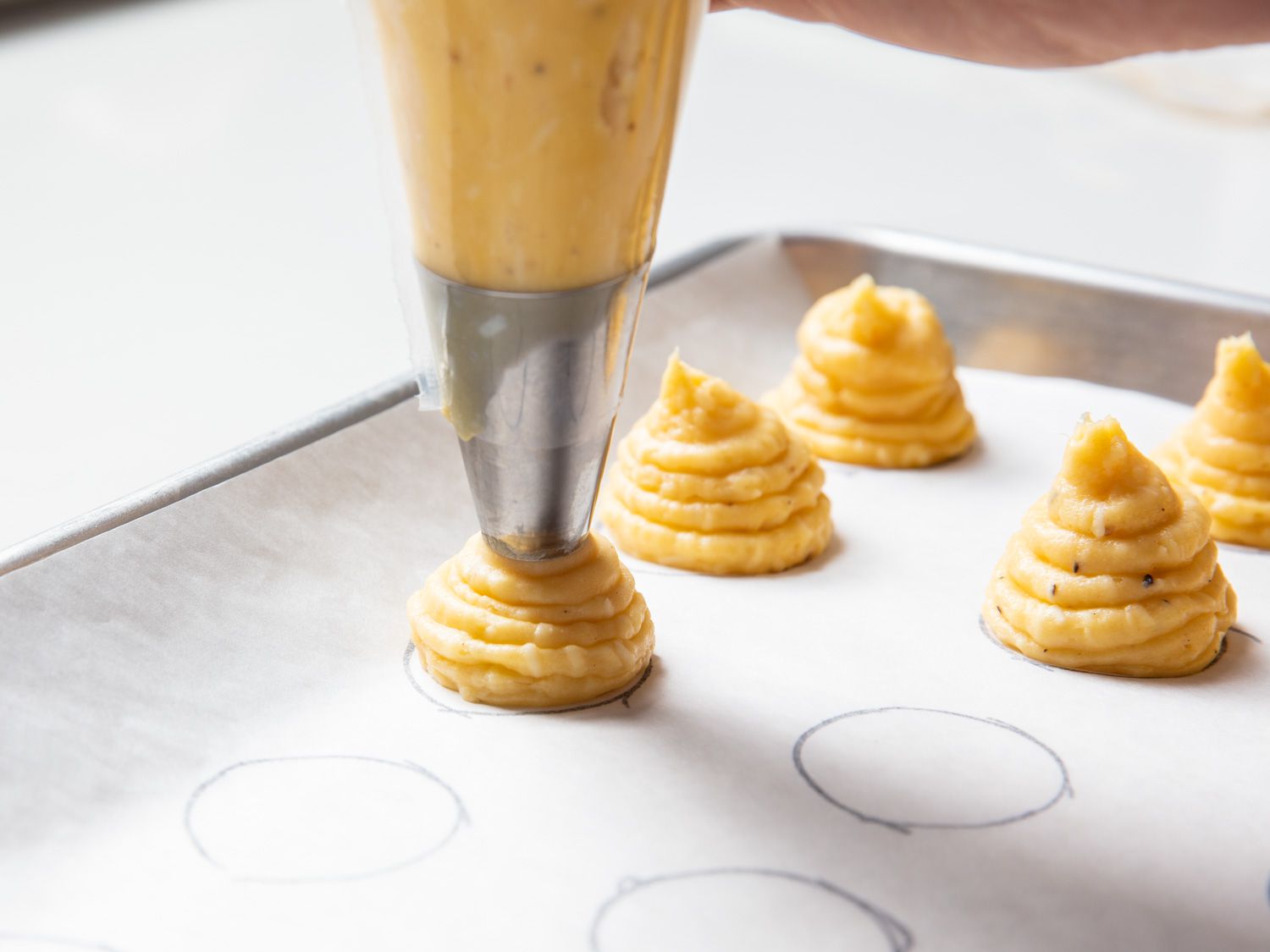 Closeup of choux paste being piped onto a parchment sheet that has been marked with 1 1/2-inch circles.