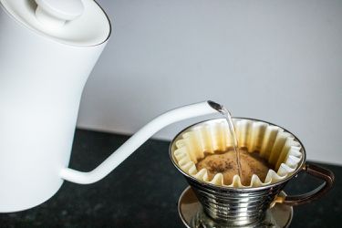 water being poured from a gooseneck kettle into a pourover coffee maker