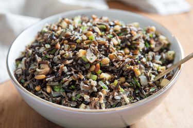 A large serving bowl containing wild rice salad with mushrooms, celery root, and pine nuts.