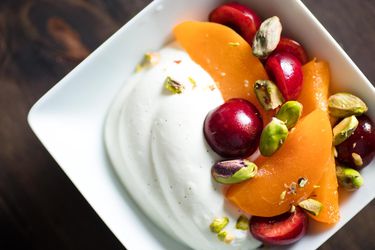 Overhead shot of a bowl of summer fruits and whipped Greek yogurt garnished with pistachios.