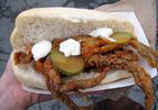 A deep fried soft-shell crab sandwich with pickle slices, mayo, and hot sauce on a split bun.