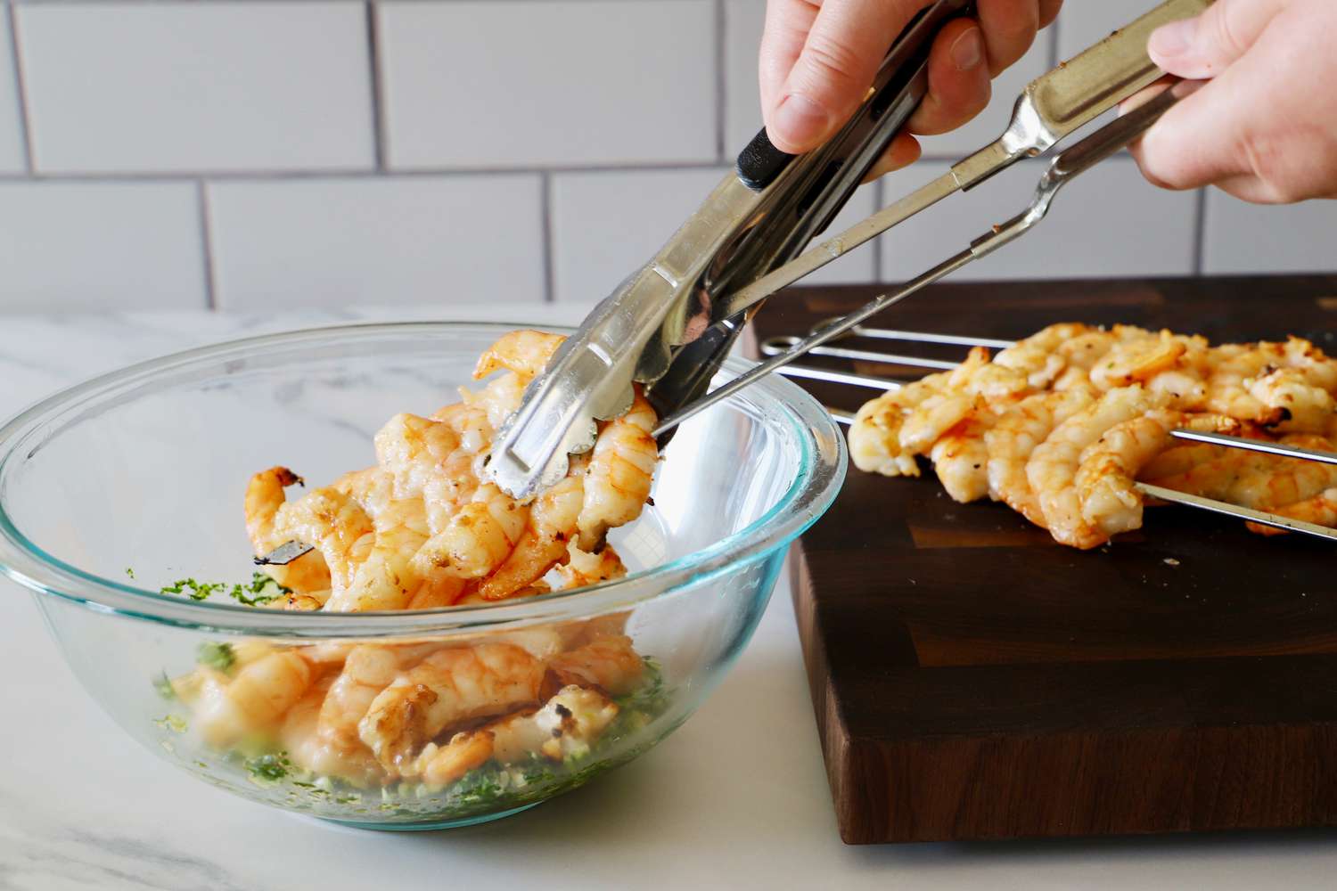 A person using tongs to remove grilled shrimp from two skewers