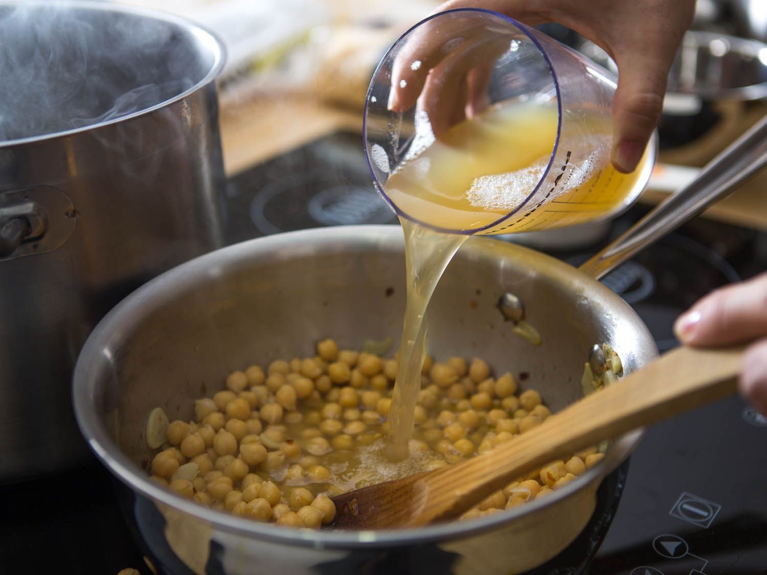 将煮豆水倒入盛有鹰嘴豆、大蒜和红辣椒碎的锅中。
