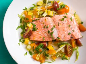 把三文鱼片放在夏季蔬菜和肉汤上轻轻煮熟