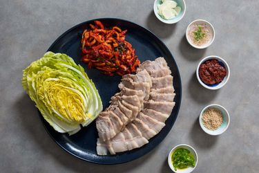 一个platter of bossam, complete with sliced pork belly, fresh cabbage leaves, and an array of condiments.