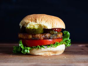 A fully dressed veggie burger on a bun with pickle, tomato, and lettuce.