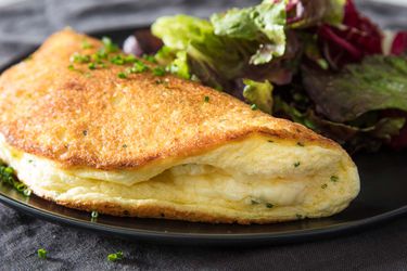 Soufflé omelette on a black plate with mixed green salad on the side.
